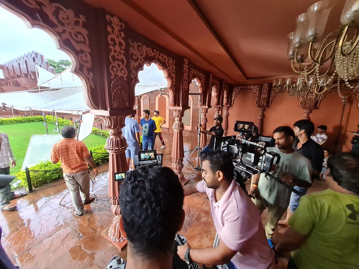 Film crew on an ornate red sandstone palace balcony, scouting the location for Nayki
