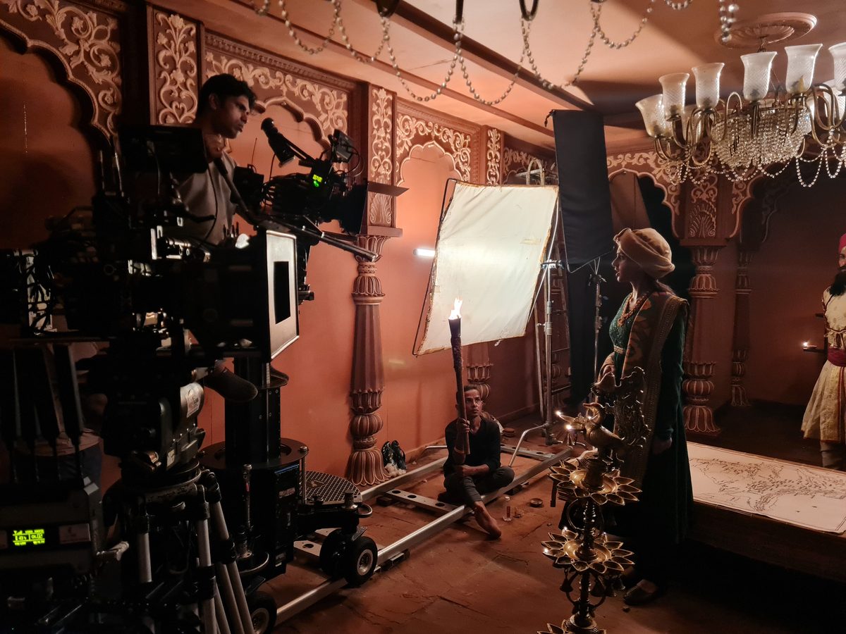 Actress in a green sari holding a lit oil lamp, filmed by the Nayki camera crew